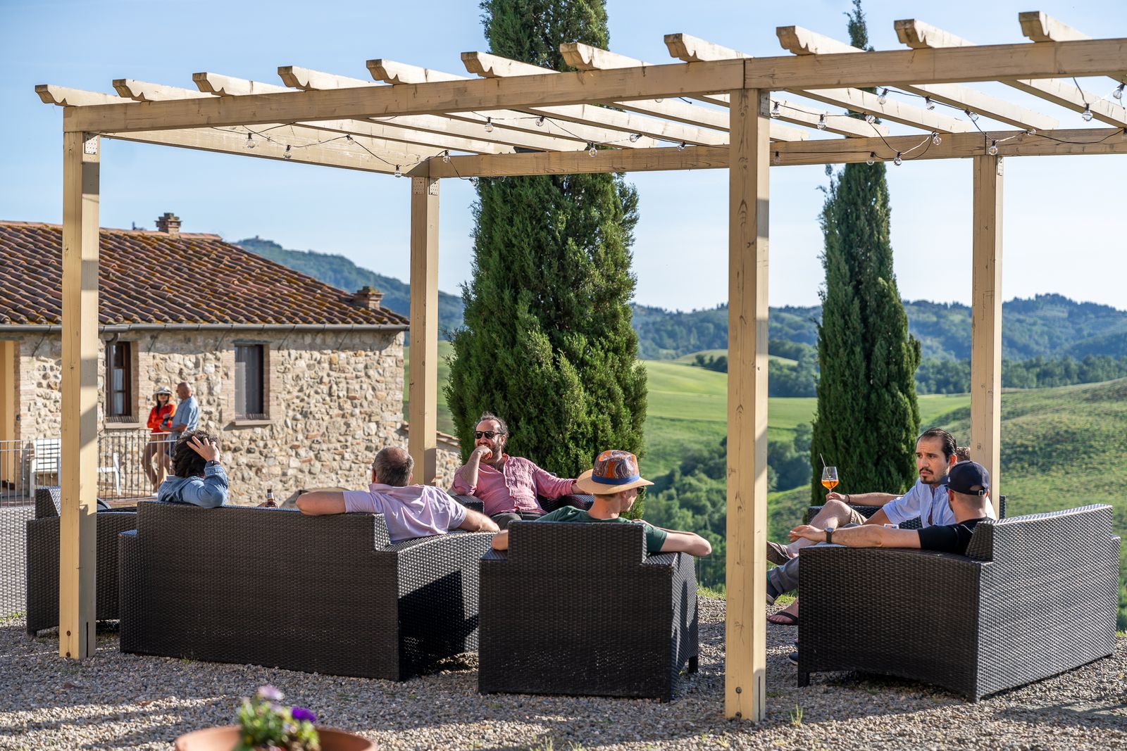 Guests having an aperitivo under the pergola, with the Tuscan hills behind