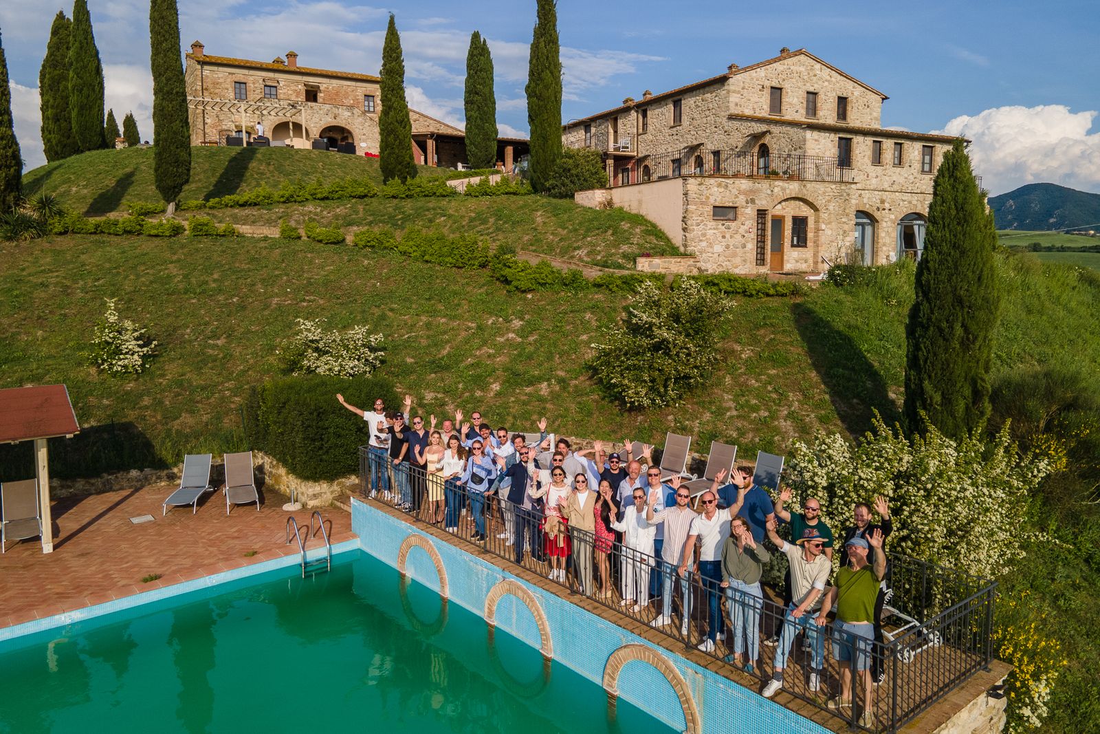 The whole group waving goodbye from the pool terrace, with the villa behind